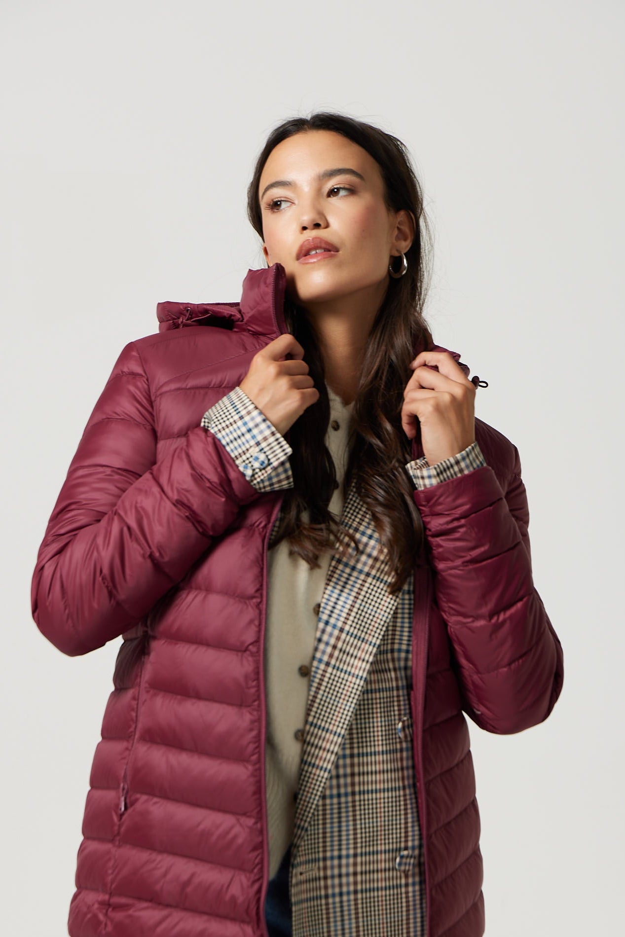 Woman wearing a burgundy puffer jacket over a plaid coat on a white background